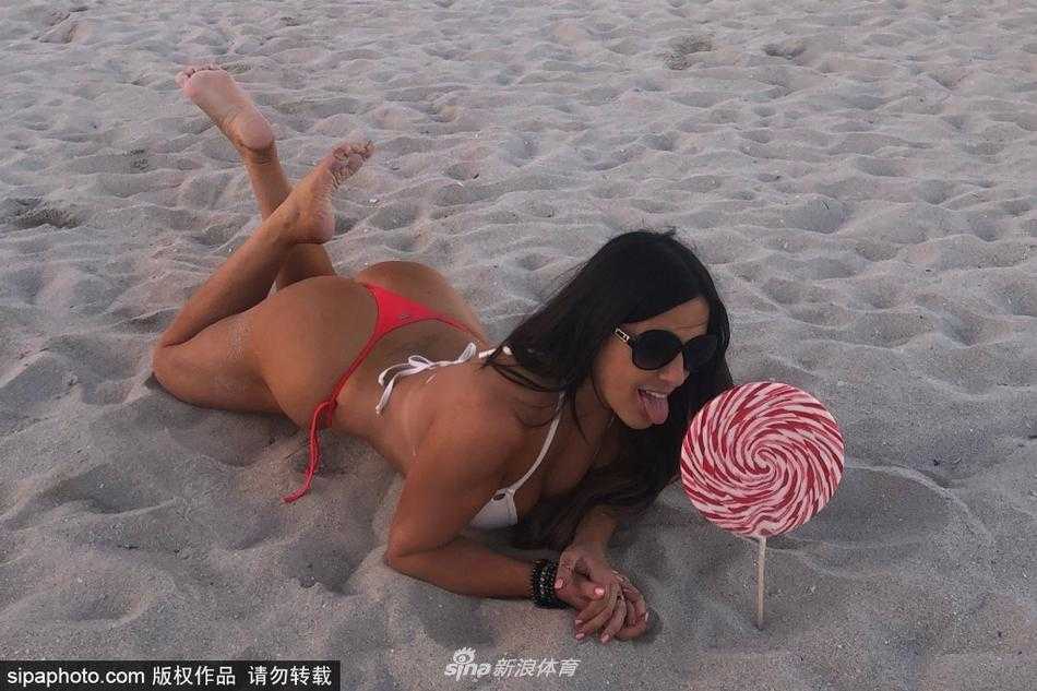 克劳迪娅侧身躺在沙滩巾上，阳光勾勒出她完美的身体轮廓，身后的海浪轻轻拍打着岸边，整个画面宁静而充满美感，她仿佛就是这片海滩上最璀璨的明珠。