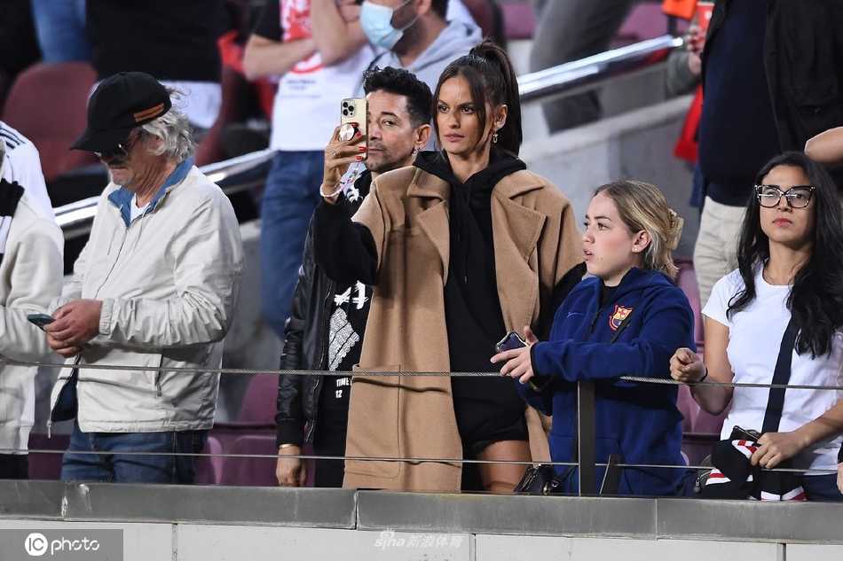 古拉特微微侧身与友人交谈，嘴角泛起一丝浅浅的笑意，场内的紧张气氛与看台上这抹轻松瞬间形成鲜明对比。