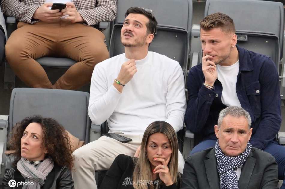 因莫比莱侧身与友人交谈，脸上带着轻松的微笑，展现出与赛场边专注观战时不同的另一面。