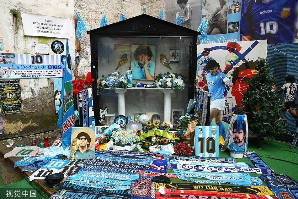 夜幕下的迭戈·马拉多纳球场外景，巨幅的马拉多纳纪念横幅在灯光下显得肃穆而温暖，球迷们聚集于此，仿佛在等待一位老朋友的归来。