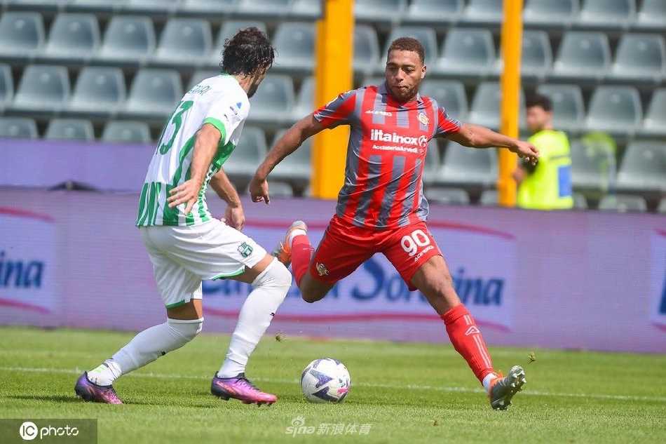 萨索洛前锋皮纳蒙蒂在克雷莫纳后卫的贴身紧逼下强行起脚射门，身体失去平衡，脸上写满了专注与不甘。